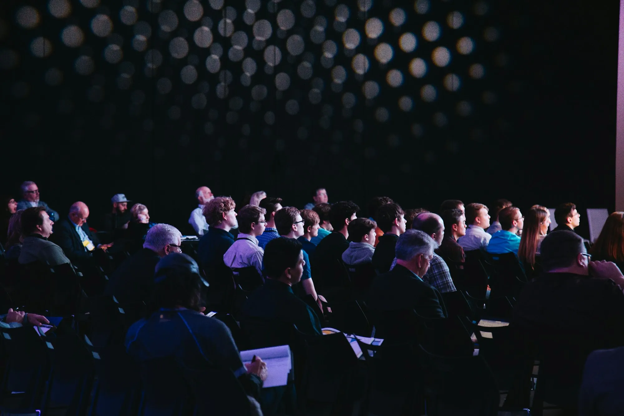 Delegates seated in a darkened auditorium, facing a lit stage.